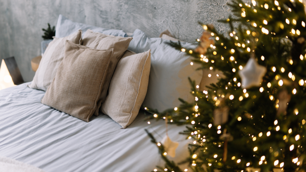 A bedroom with cushions on the bed and a lit Christmas tree