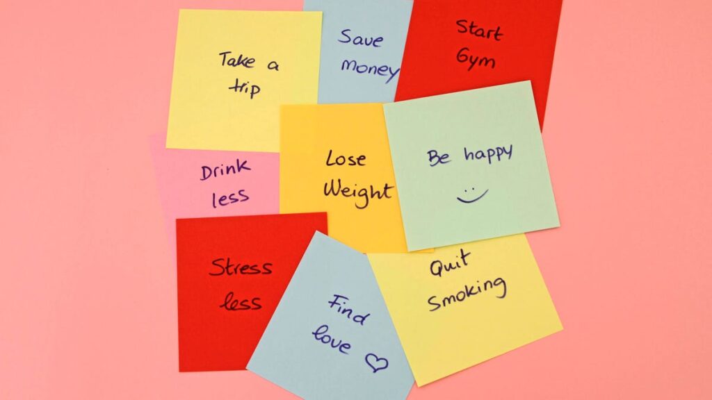 Different New Year's resolutions listed on sticky notes over a coral-colored background.