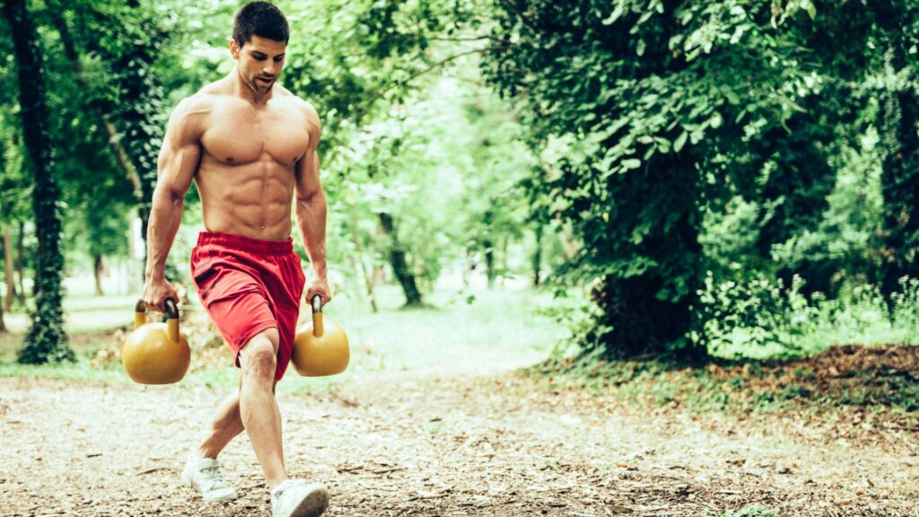 Forget long gym sessions: This 7-7-7 kettlebell workout builds full-body strength in half the time Man walking through a park holding two kettlebells performing a farmer's walk