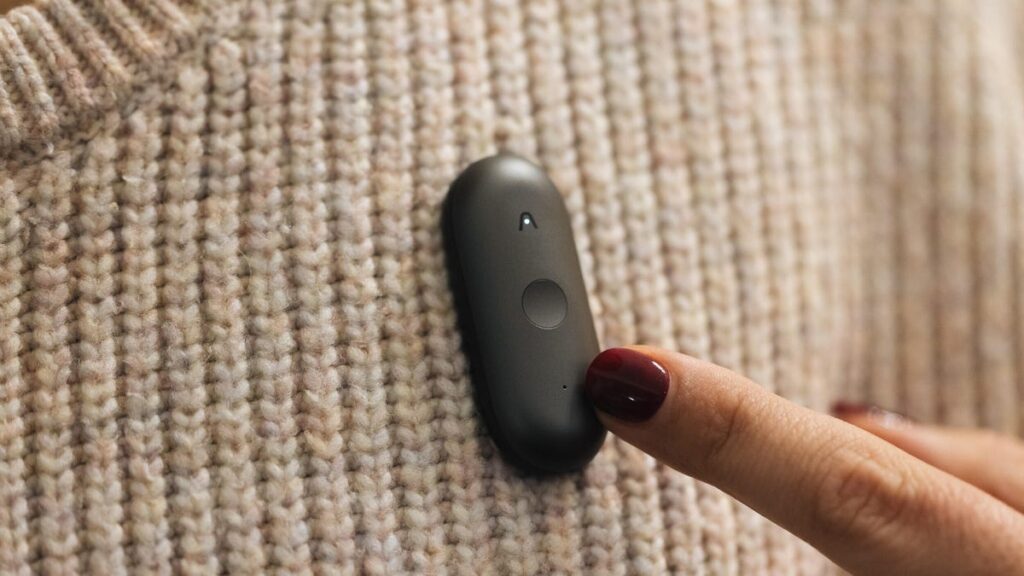 A Plaud AI pin is attached to a brown sweater.