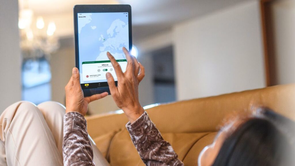 Norton VPN: 2025’s milestones and the roadmap for 2026 A woman laying back on a sofa and using Norton VPN on her tablet.