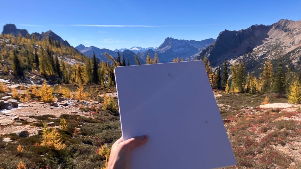 A hand holding a Starlink mini dish with mountains in background