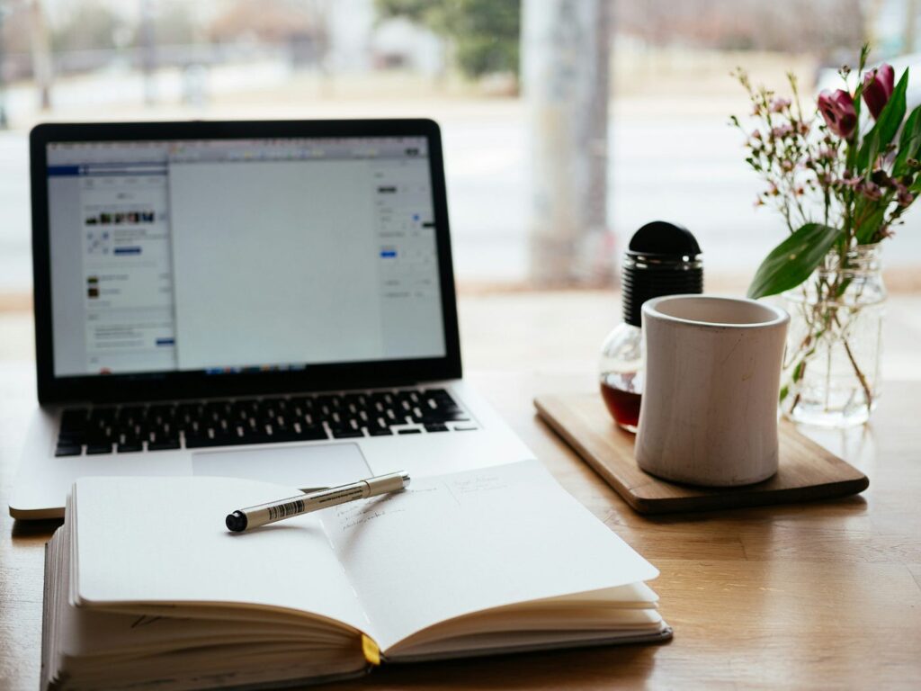 Laptop, notebook, and coffee cup on desk. Photo by Nick Morrison on Unsplash