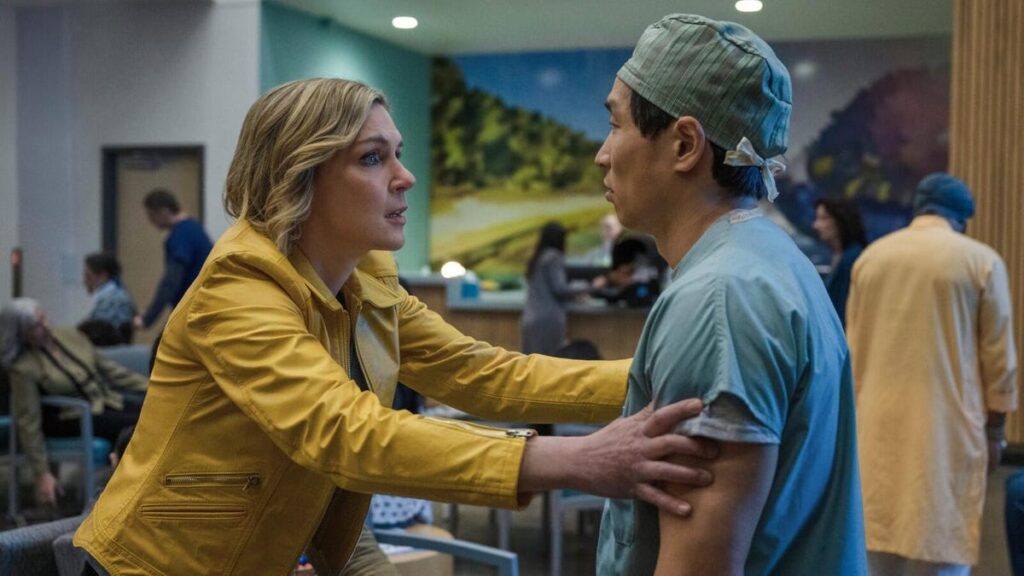 A still from Pluribus featuring Seehorn's character grabbing the arms of a medical professional who is in scrubs.