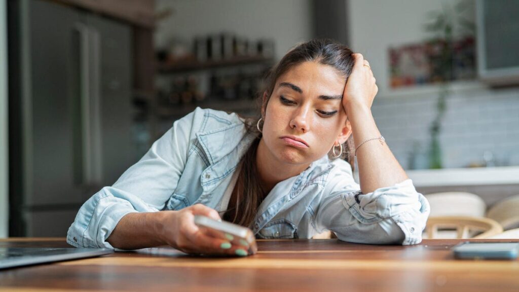 When Your Phone Pings, It Hijacks Your Brain for 7 Seconds, Study Finds An annoyed person leans on a table and looks at the phone they're holding.