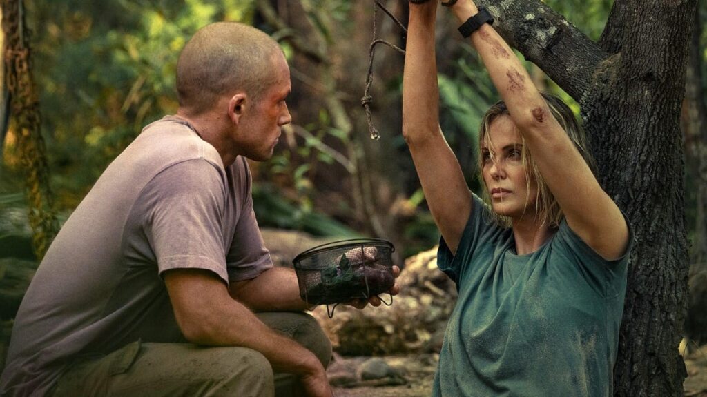 Production still from Apex showing Charlize Theron tied to a tree and Taron Egerton with a shaved head terrorizing her.