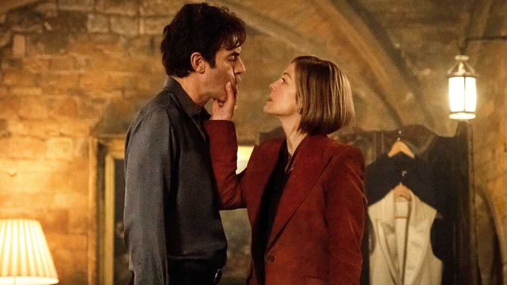 Rosamund Pike holds Sacha Baron Cohen's face