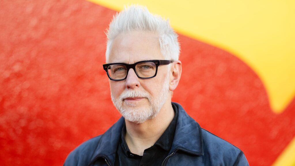 A close up of James Gunn standing in front of a giant Superman logo
