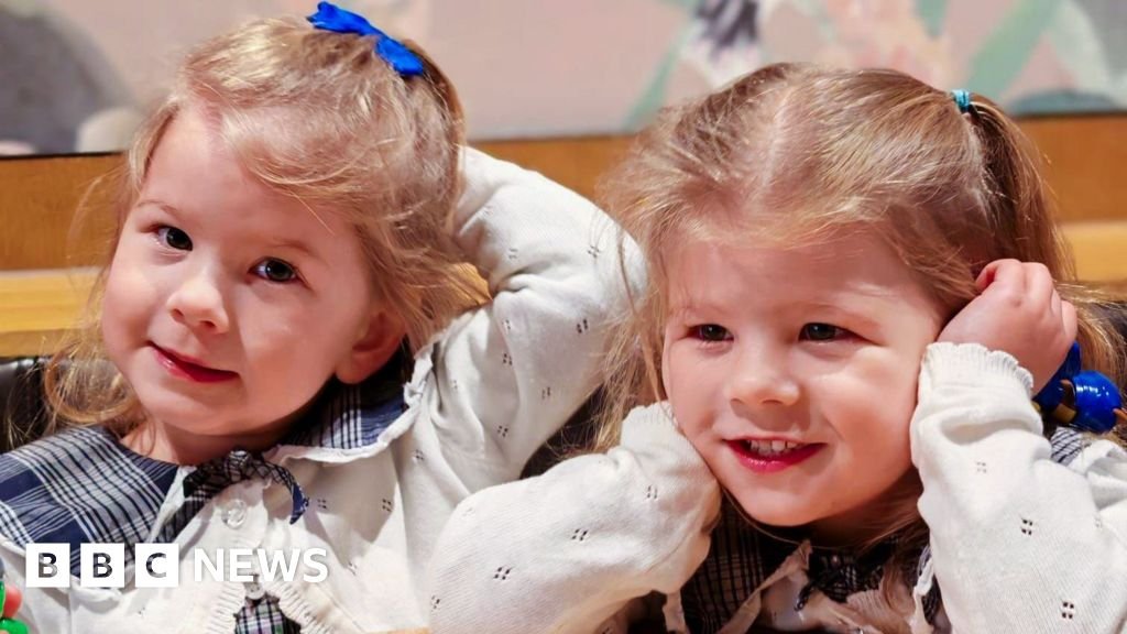 Pioneering treatment saves twins in early pregnancy Nancy and Margo are photographed close up - their faces and blond hair in bunches are visible, and they are smiling. They are wearing the same clothes - a blue blouse and white cardigan.
