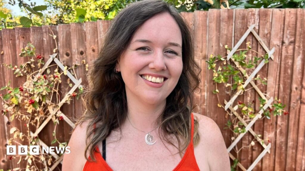 A white woman with brown hair smiles in the garden looking at the camera.