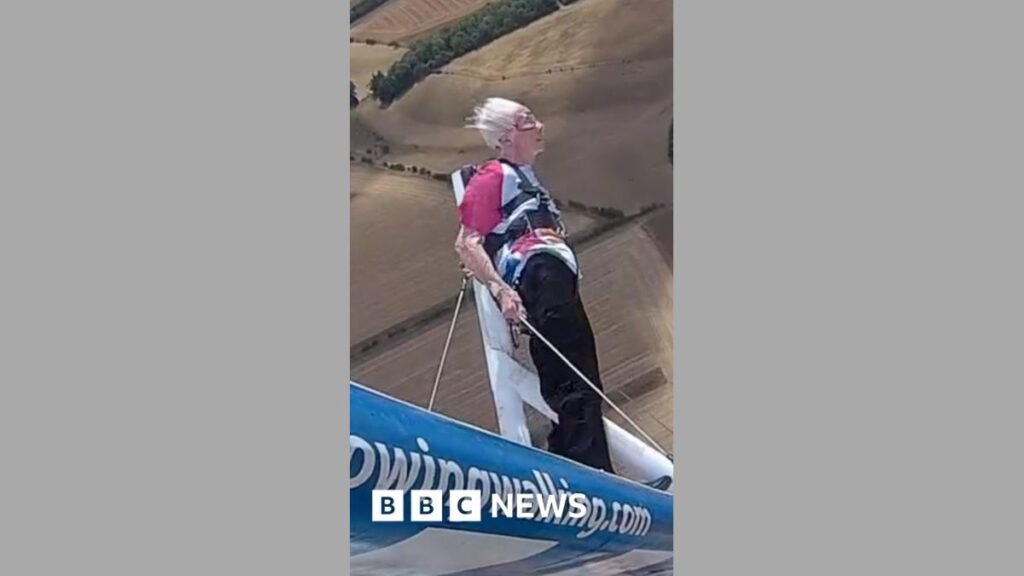 Woman wingwalking mid-air with her hair blown back by the wind.