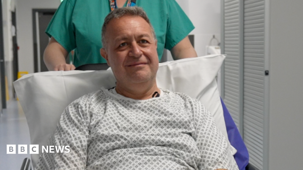Brain tumour diagnosis cut from weeks to hours with rapid new NHS test Steve wears a hospital gown and sits up on a gurney. He is propped up on a pillow and is wearing a patterned hospital gown in black and white. He is being pushed on his way to have his operation