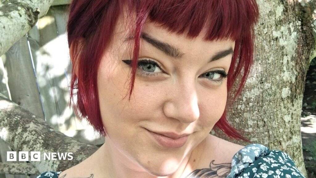 Endometriosis trial gives hope to millions of women in pain like me A woman, Charlotte McCann, smiling at the camera, she is wearing a floral top, and she has tattoos visible just below her shoulders.