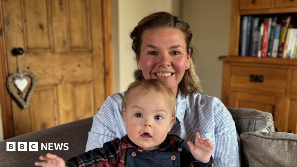 Emma with her son Bert, who's holding his hands up. She is smiling and has her hair tied back, wearing a blue and white striped shirt.